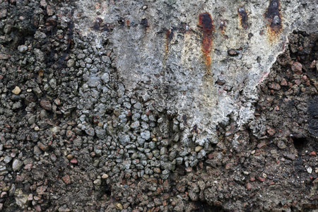 Close-up of weathered reinforced concrete with exposed aggregate and vertical rust stains. Rugged...