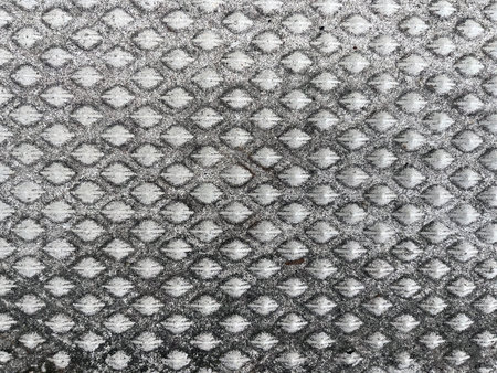 Close-up of a textured metal surface with a repeating diamond-shaped pattern, showing signs of wear...