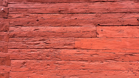 Close-up of a weathered red wooden wall with horizontal planks, showing peeling paint, rough texture, and rustic aged appearance.の写真素材