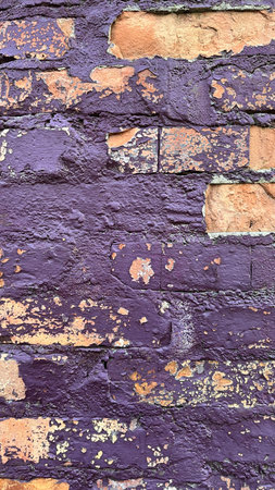 Close-up of a weathered brick wall with peeling purple paint revealing orange bricks beneath, creating a textured and rustic surface.の写真素材
