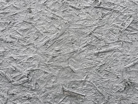 Close-up of a gray textured surface resembling rough plaster or concrete with embedded wood fibers, creating an abstract industrial pattern.の写真素材
