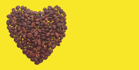 Heart of coffee beans on a yellow background. Copy spaceの写真素材