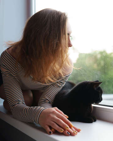 girl in a skirt and a cat are sitting on the window on the street evening artの写真素材