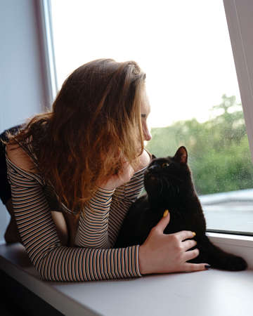 girl in a skirt and a cat are sitting on the window on the street evening artの写真素材