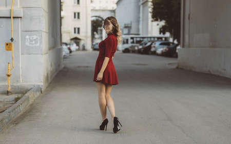 Nice tanned stylish brunette girl in red short dress with flowers is standing poses and flirting walking on the street cityの写真素材
