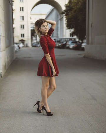 Nice tanned stylish brunette girl in red short dress with flowers is standing poses and flirting walking on the street cityの写真素材