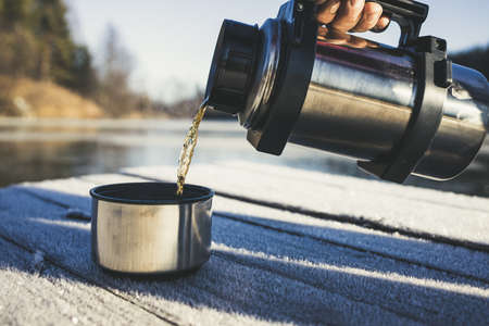 Pours hot tasty tea from a flask in the winter into the cold.の写真素材