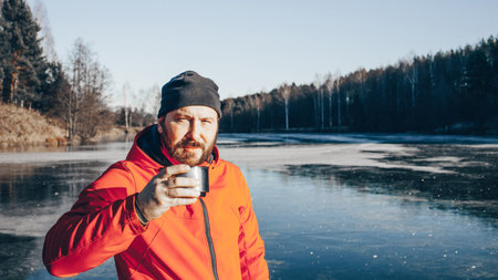 A lone tramp traveler stands on ice and drinks tea from a thermoの写真素材