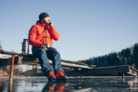 A lone tramp traveler stands on ice and drinks tea from a thermoの写真素材