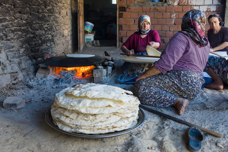 EVRENLERYAVSI, TURKEY - JUNE 24, 2014: Village women prepare traditional flatbread on an open fire.のeditorial素材