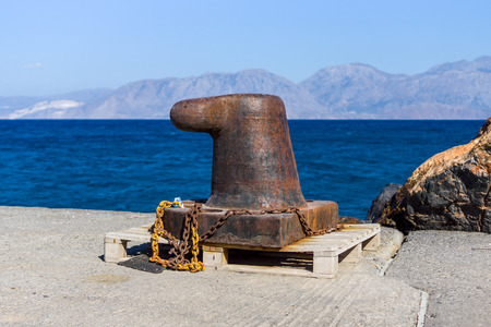 Rusty bitt with a chain on the berth. In the background of sea and mountains.