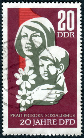 GERMANY - CIRCA 1967: A stamp printed in Germany (GDR), dedicated to 20th Anniversary of Democratic Women's Federation of Germany, shows the woman with child, circa 1967のeditorial素材