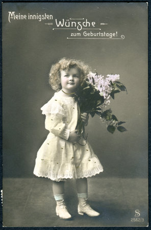 SWITZERLAND - CIRCA 1911: A greeting postcard printed in Switzerland, shows a girl with a bouquet of lilacs. The inscription in German: Happy birthday, circa 1911のeditorial素材