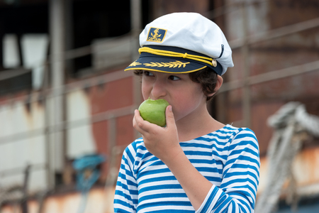 Portrait of a boy in a vest (Telnyashka) and captain's cap. In his hand a green apple.の写真素材