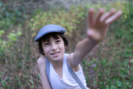 A joyful boy in a T-shirt and suspenders extends his hand forward.の写真素材
