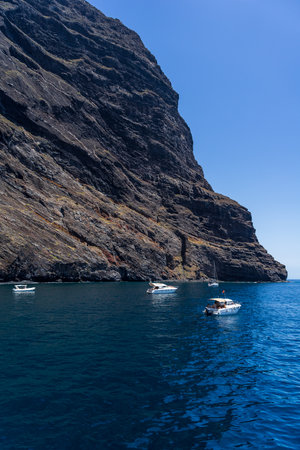 TENERIFE, CANARY ISLANDS, SPAIN - JULY 26, 2018: Yachts and boats of tourists near the vertical cliffs Acantilados de Los Gigantes (Cliffs of the Giants). View from Atlantic Ocean.のeditorial素材