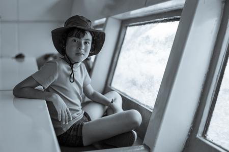 The boy is watching the underwater world through the large porthole below of  the waterline a tourist ship. Black and white.の写真素材