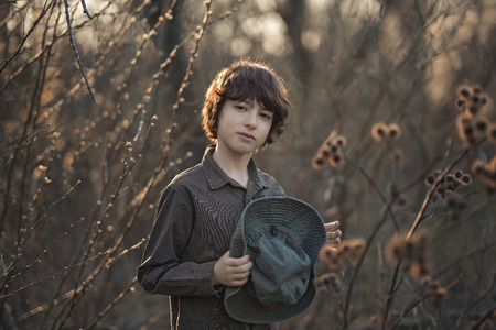 A boy in a hat and coveralls is standing in dry bushes of burdock.の写真素材