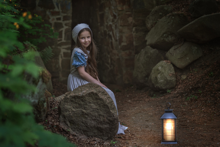 A girl in retro clothes stands with a lantern near the fortress wall.の写真素材