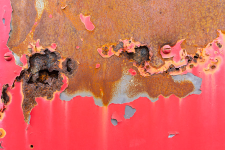 Rusty metal surface with traces of aged and cracked red paint.