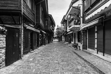 NESSEBAR, BULGARIA - JUNE 22, 2019: Beautiful and narrow street with restaurants, cafes and shops of the ancient seaside town. Deserted streets in the early morning. Black and white.のeditorial素材