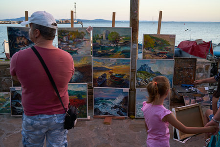 POMORIE, BULGARIA - JUNE 30, 2019: Promenade with tourists on the shore of the seaport of the seaside resort town of Pomorie. Gallery of paintings by local artists.のeditorial素材