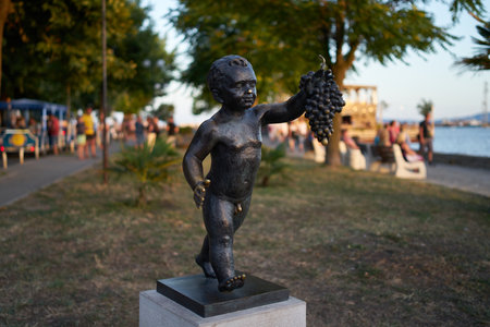 POMORIE, BULGARIA - JUNE 30, 2019: Bronze sculpture of a boy with a bunch of grapes on the embankment of the seaside town.のeditorial素材