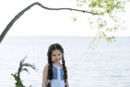 Portrait of a beautiful little girl with long hair near the lake on a sunny day.の写真素材