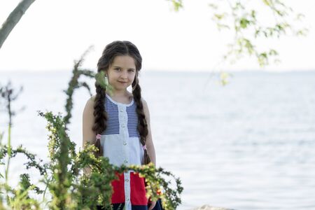 Portrait of a beautiful little girl with long hair near the lake on a sunny day.