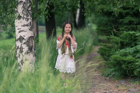 Portrait of a little beautiful girl in a birch grove. Her shoulders are covered with a shawl with traditional Russian folk patterns.の写真素材