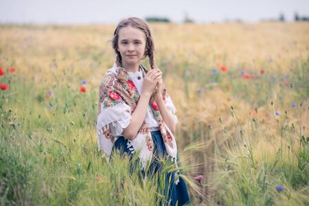 Portrait of a beautiful girl in a field with wild flowers. Her shoulders are covered with a shawl...