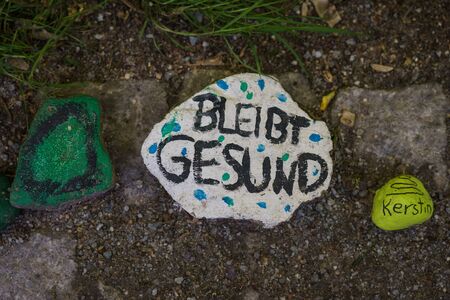 A new trend in Berlin, Germany - children lay colored stones along park paths in support of doctors fighting the new coronavirus COVID-19. The inscription in German: Stay healthy.の写真素材