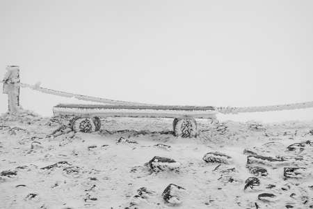 Frost-covered frozen wooden bench. Black and white.