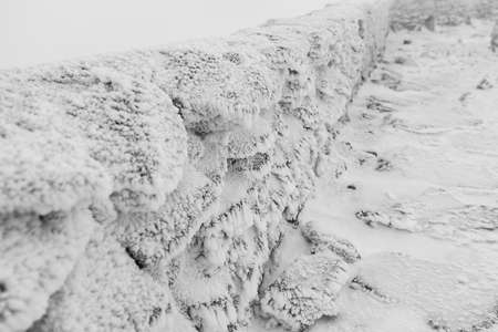 A stone fence covered with ice and snow. Focus on the foreground. Black and white.の写真素材