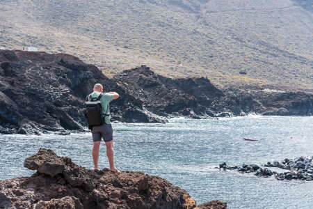 Photographer on the edge of a cliff against the backdrop of the ocean and mountains.の写真素材