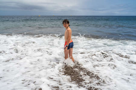 A teenager is standing on the sandy shore of the ocean.の写真素材