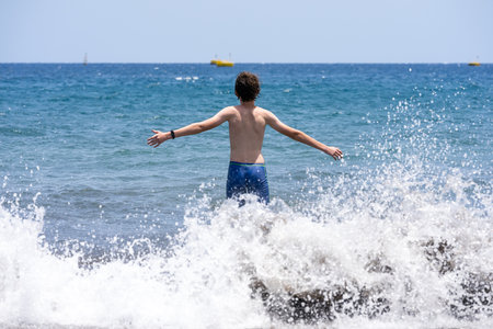 A teenager is standing on the sandy shore of the ocean.の写真素材