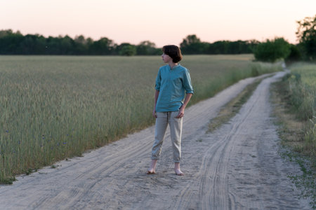 A barefoot teenager in comfortable clothes stands on a dirt road.の写真素材