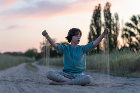 A barefoot teenager in comfortable clothes sits on a dusty dirt road.の写真素材