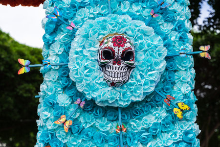 GARACHICO, TENERIFE - AUGUST 5, 2025: Decorative skull mask surrounded by blue paper flowers and colorful butterflies during Fiesta de la Muerte street celebration. Canary Islands.のeditorial素材
