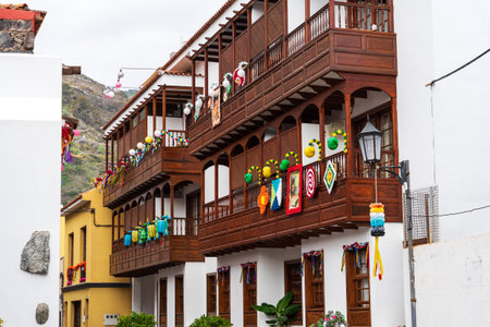 GARACHICO, SPAIN - AUGUST 5, 2025: Traditional wooden balconies decorated with colorful festival ornaments on residential building facade. Tenerife, Canary Islands.のeditorial素材