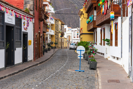 GARACHICO, SPAIN - AUGUST 5, 2025: Curved cobblestone street with decorated traditional houses, potted plants and parked car in historic town center. Tenerife, Canary Islands.のeditorial素材