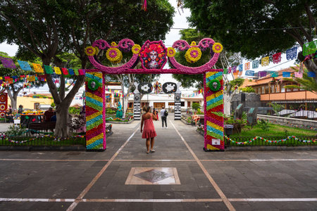 GARACHICO, TENERIFE - AUGUST 5, 2025: Colorful Fiesta de la Muerte entrance arch with paper flowers, skull motifs and visitors walking in decorated town square, Canary Islands.のeditorial素材