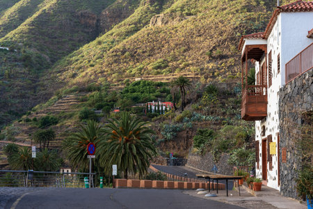 MASCA, TENERIFE - AUGUST 5, 2025: Mountain road with palm trees, terraced slopes and traditional house with wooden balcony in rural valley, Canary Islands.のeditorial素材