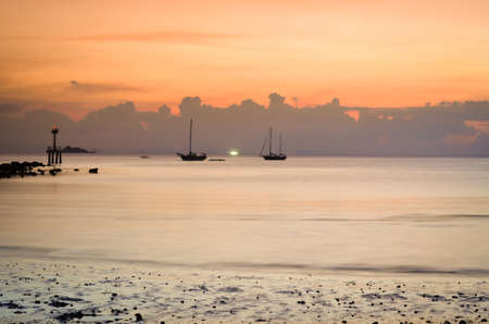 dramatic sunset at tropical beach with boat silhouettesの写真素材
