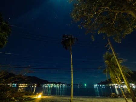 stars at nightsky with palmtrees and campfire near villageの写真素材