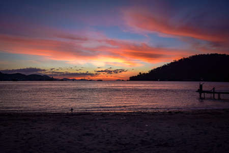 tropical sunrise with woman standing on jetty and enjoying liveの写真素材