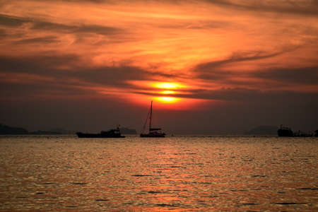 sun rises behind sailing boat with dramatic colors and cloudsの写真素材