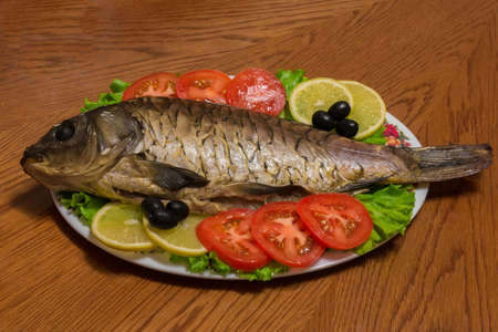 The photo shows a fish on a plate with tomatoes and olivesの写真素材