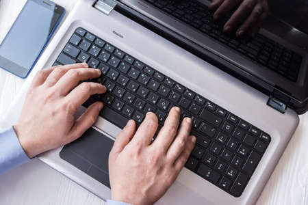 man behind laptop with smartphone in office